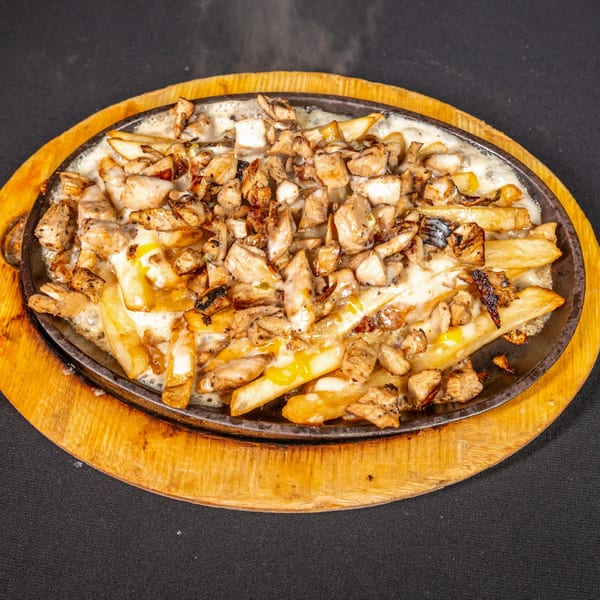 Sizzling skillet of El Paso Mexican Grill's chicken and fries covered in melted cheese, on a wooden board.