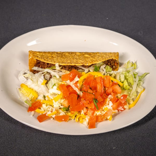 A crispy beef taco with lettuce, tomatoes, and shredded cheese on a white plate.