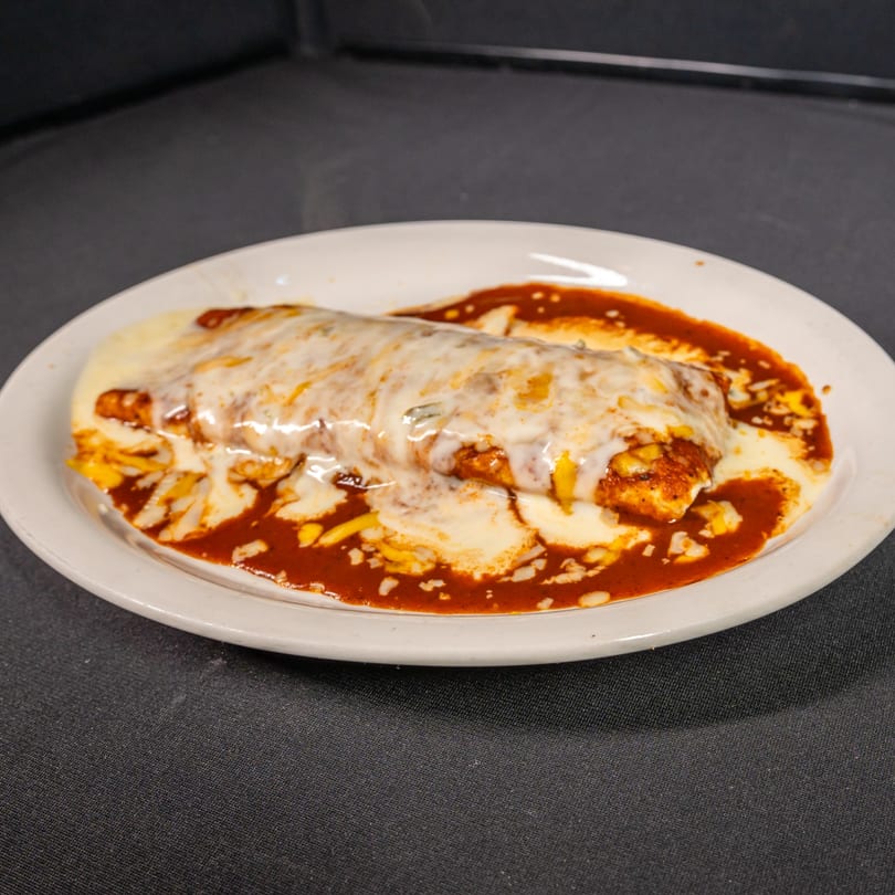 A large, cheesy burrito covered in red sauce and white cheese on a white plate.