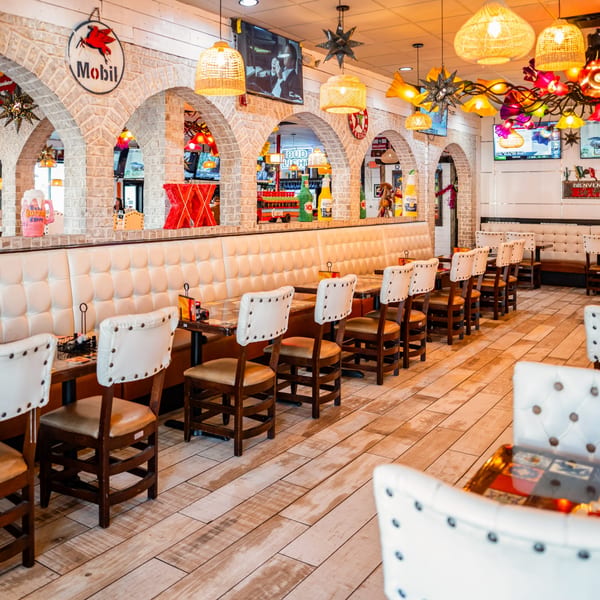 El Paso Mexican Grill dining room with white booths, wooden chairs, brick arches, and colorful decor.