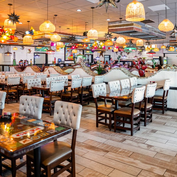 Colorful Mexican restaurant interior with decorative lighting, white tufted booths, and patterned tables.