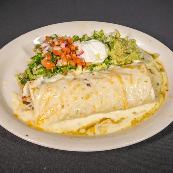 A large, cheese-covered burrito with sides of pico de gallo, sour cream, and guacamole.