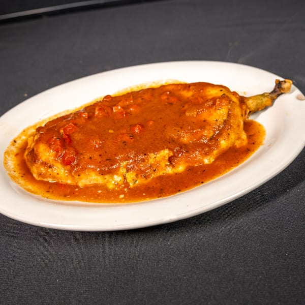 A chile relleno, covered in red sauce with diced tomatoes, on a white oval plate.
