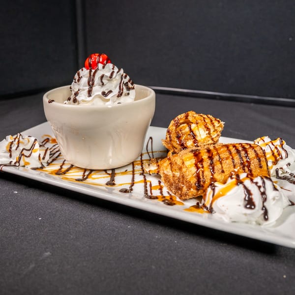 Fried ice cream and chimichanga dessert with whipped cream, chocolate, and caramel drizzle on a white plate.