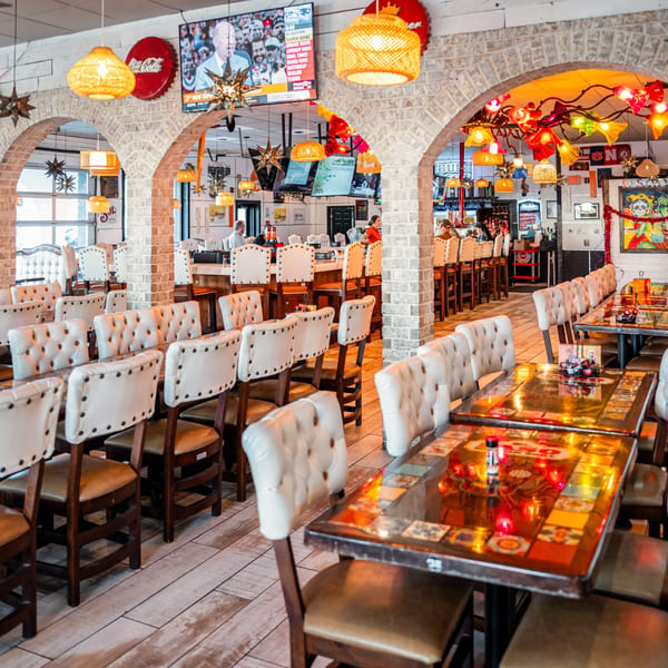 Spacious El Paso Mexican Grill dining room with white tufted chairs, brick arches, and colorful decor.