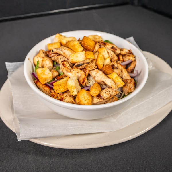 Grilled chicken and croutons in a white bowl, served on a plate with parchment paper.
