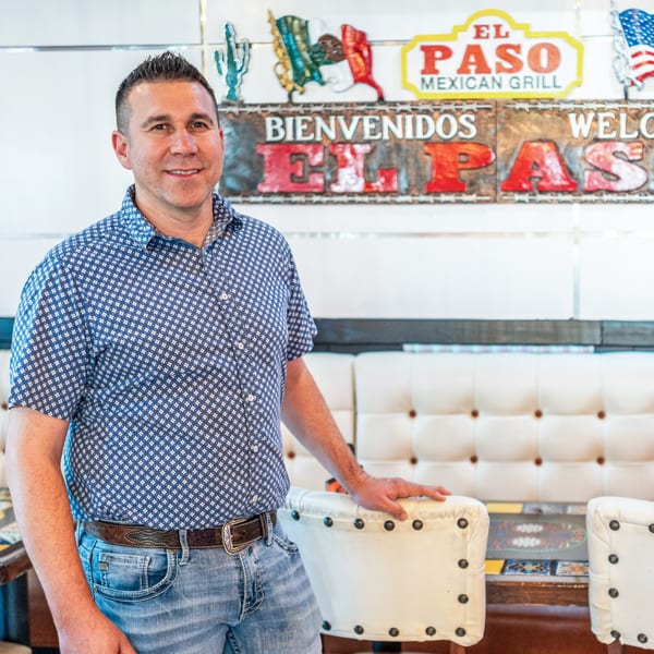 Man in a blue patterned shirt and jeans standing in front of El Paso Mexican Grill signage.